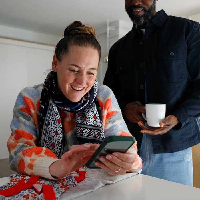 Woman consulting the mobile with a man in the background holding a cup